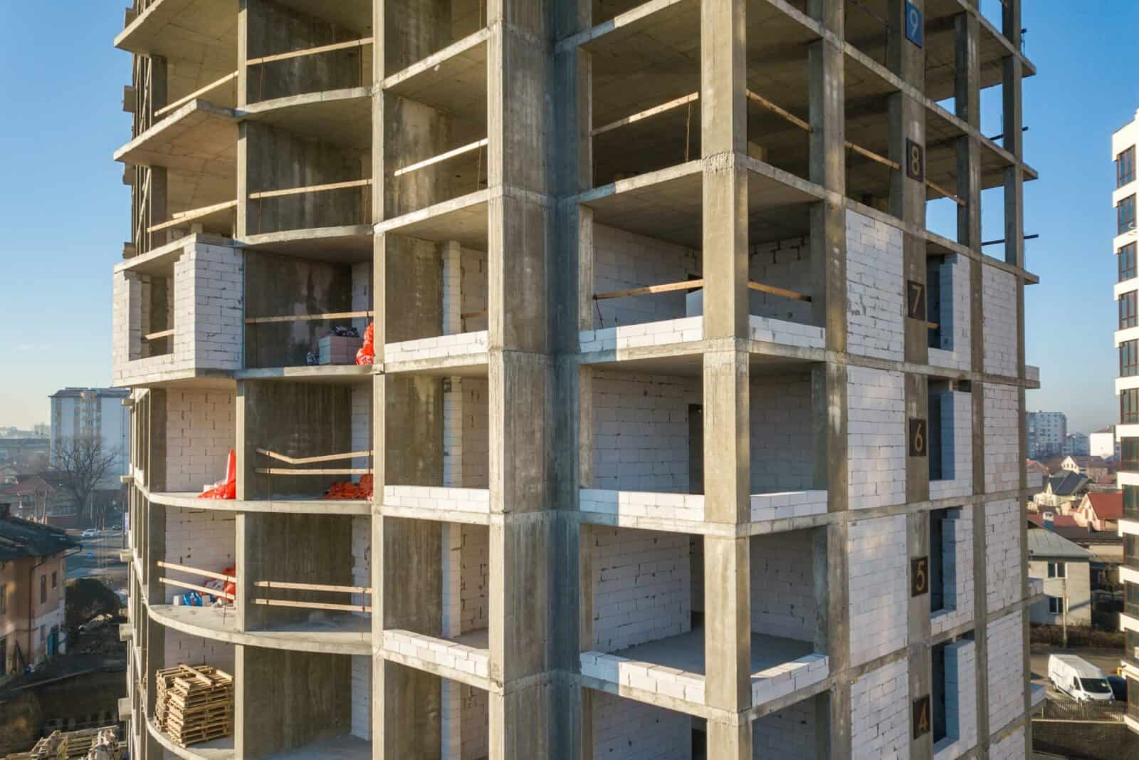 Aerial view of concrete frame of tall apartment building under construction in a city.