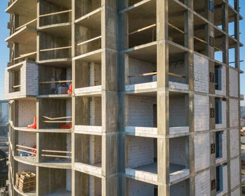 Aerial view of concrete frame of tall apartment building under construction in a city.