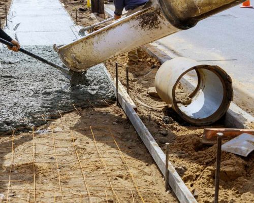 Mixer truck pouring cement concrete casting on reinforcing metal bars of sidewalk